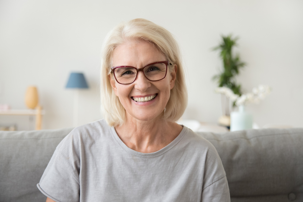 Smiling middle aged mature grey haired woman looking at camera, happy old lady in glasses posing at home indoor, positive single senior retired female sitting on sofa in living room headshot portrait. emergency electrical service